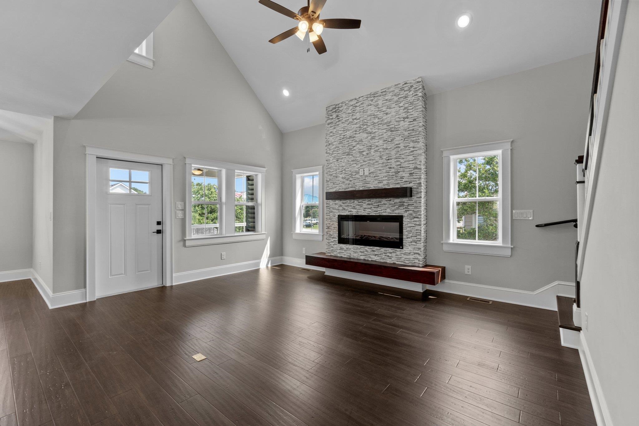 Vacant living room with vaulted ceiling, dark wood floors, and a tall stone fireplace.