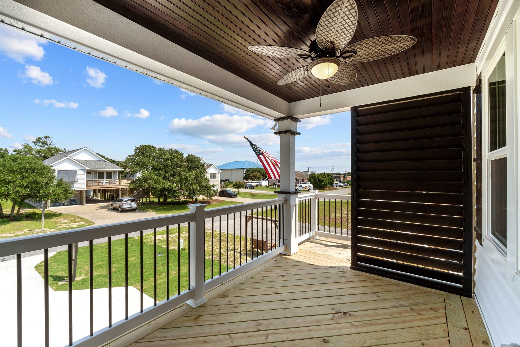 Covered wooden porch overlooking a residential street, with a ceiling fan and louvered privacy screen.