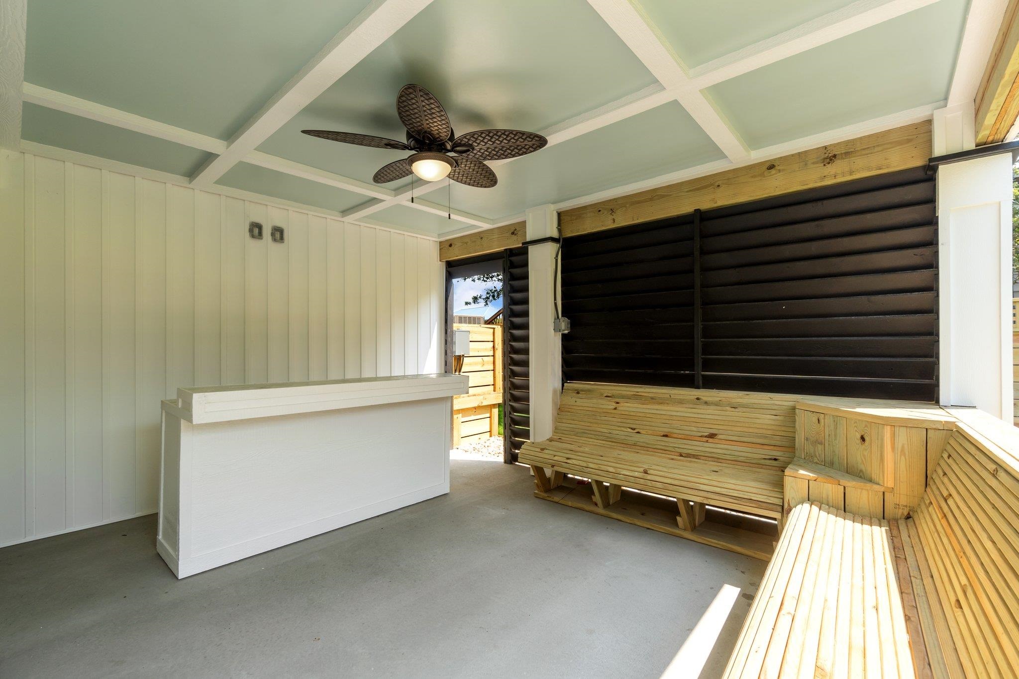 Covered porch with built-in wooden benches, a white counter, and a decorative ceiling fan.