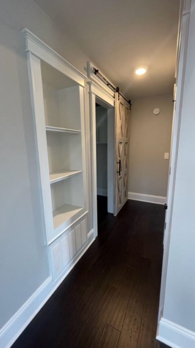 Hallway with white built-in shelves, a sliding barn door, and dark wood flooring.