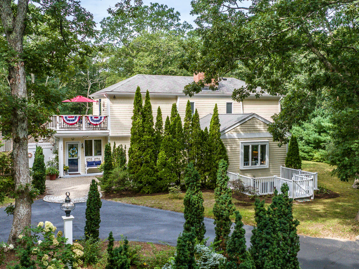 Two-story home partly screened by evergreens, with a balcony and small fenced deck.