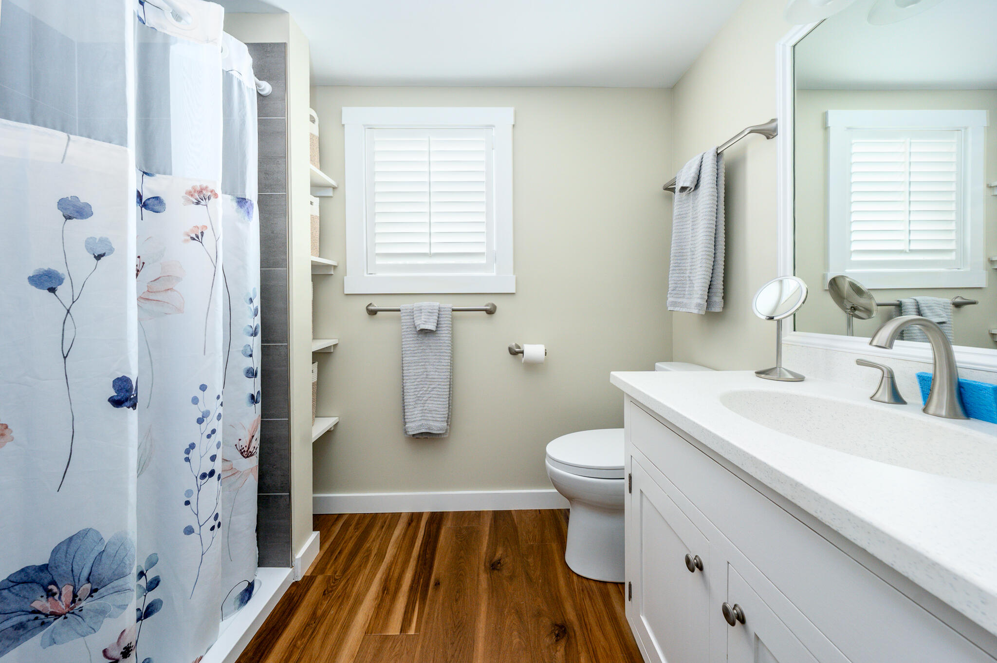 Bathroom with white vanity, shuttered window, and floral shower curtain.