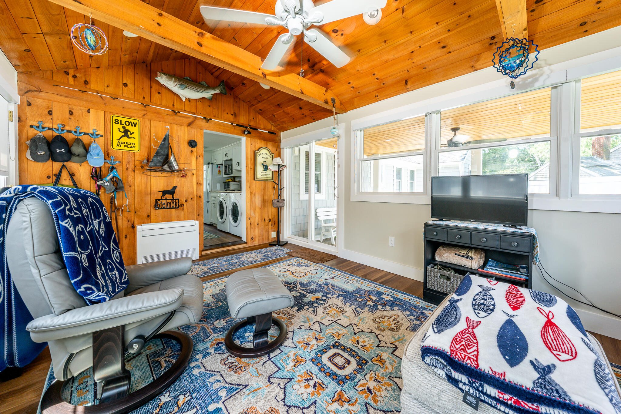 Living room with a vaulted wood ceiling, gray recliners, patterned rugs, and wide windows.