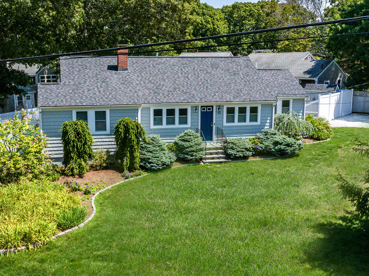 Blue-gray shingle house with a dark blue door, landscaped shrubs, and a broad lawn.