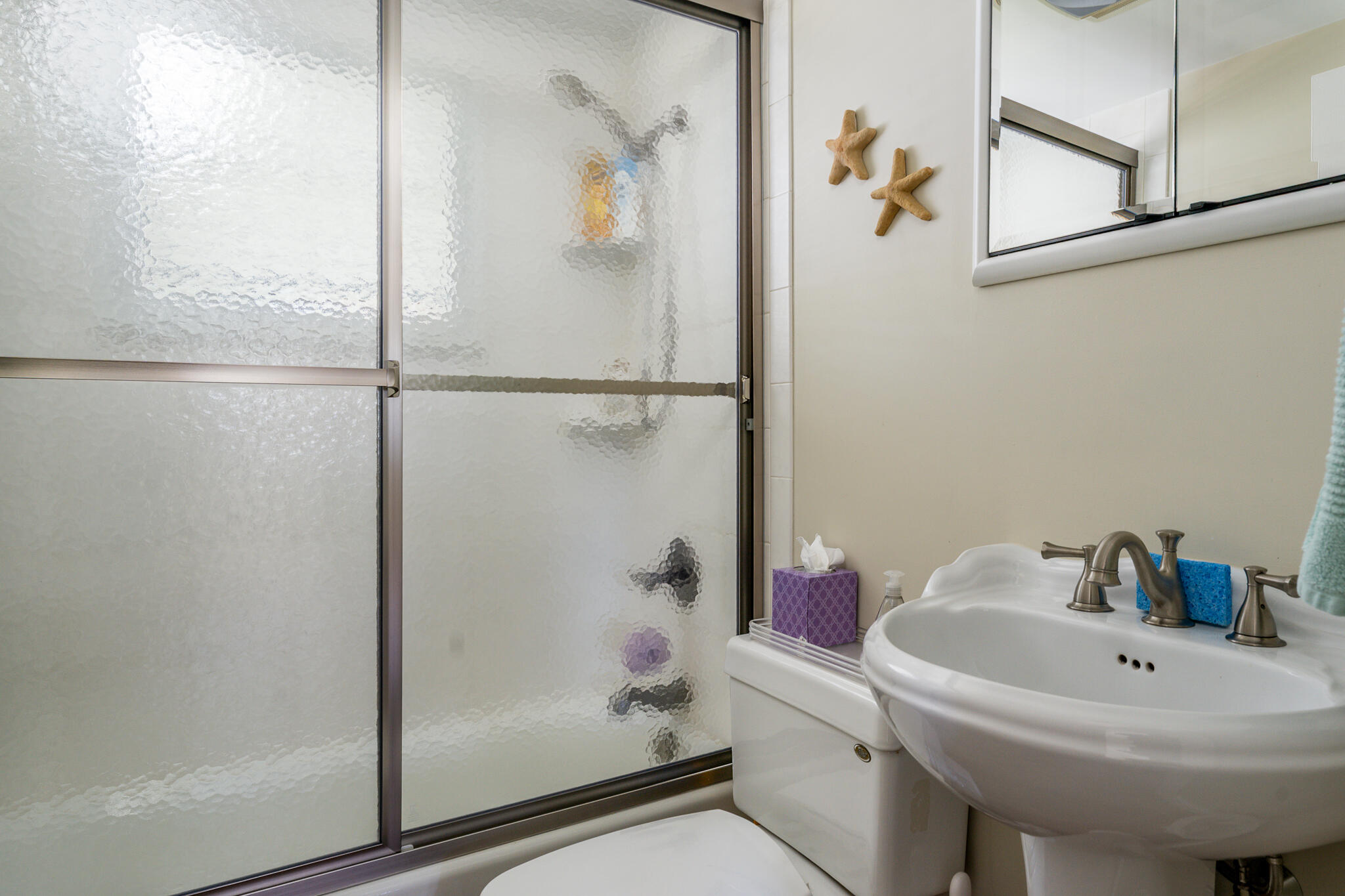 Bathroom with a frosted-glass shower, pedestal sink, and wooden starfish wall decor.
