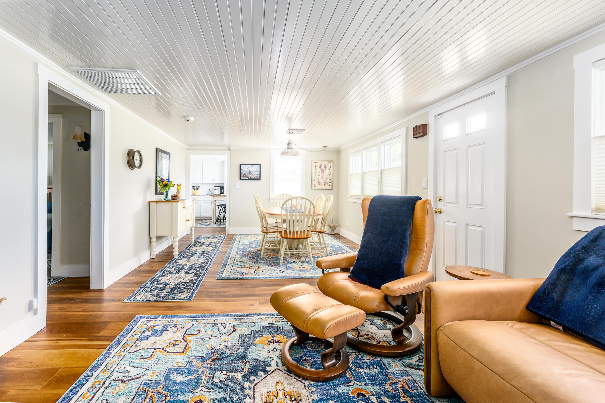 Open living and dining area with tan leather recliners, patterned rugs, and the kitchen beyond.