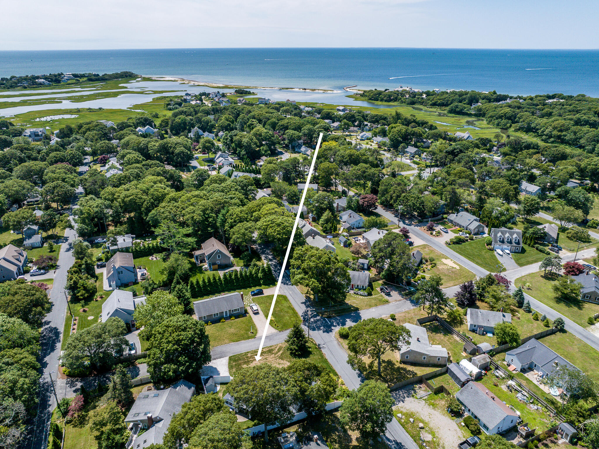 Aerial view of a coastal neighborhood, with an arrow marking the property near marshland and ocean.