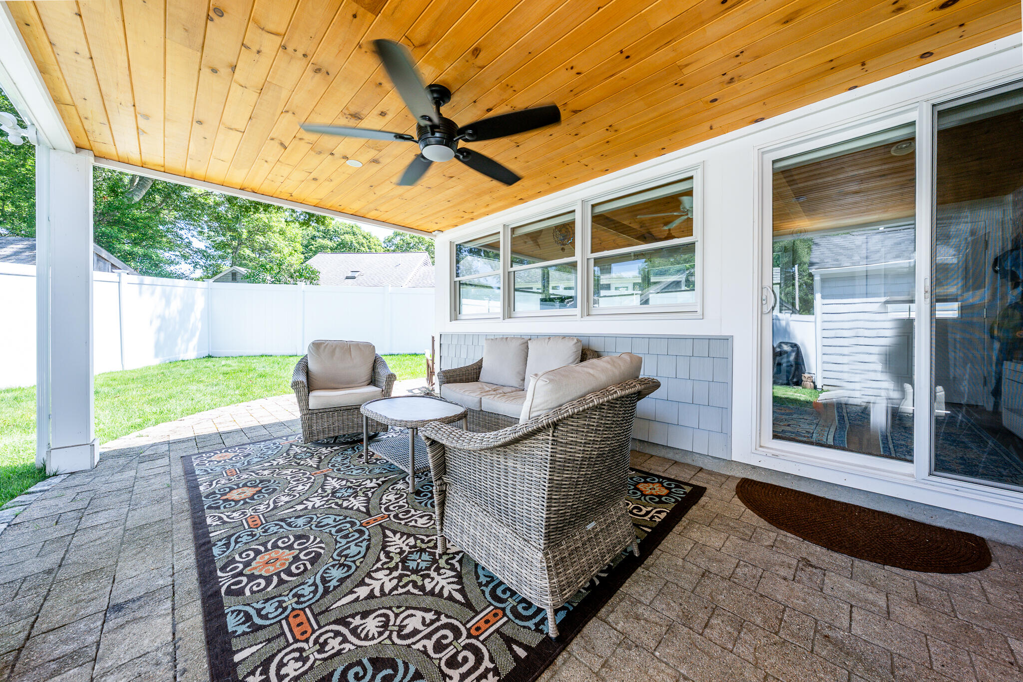 Covered patio with wicker seating, a wood-plank ceiling, and a fenced green yard.