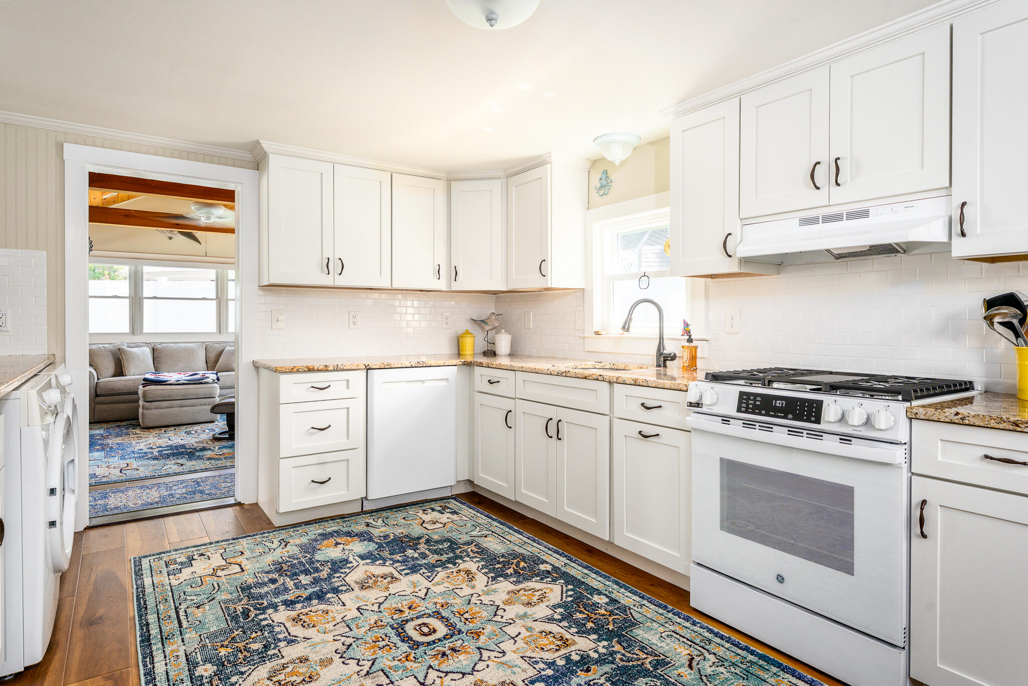 Bright white kitchen with granite counters, a gas range, and a patterned blue rug.