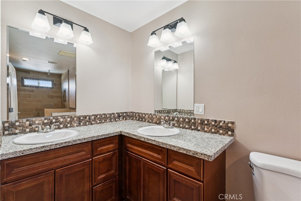 Bathroom with a double vanity, granite countertops, dark wood cabinets, and a tiled backsplash.