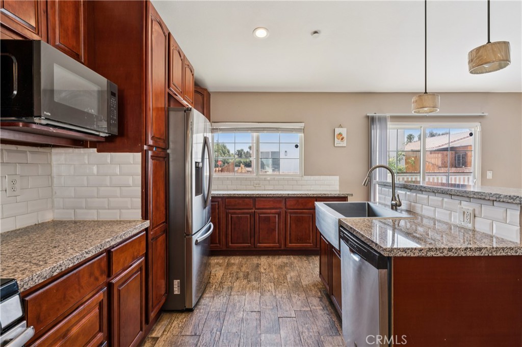 Kitchen with reddish-brown cabinets, granite counters, stainless steel appliances, and a central sink island.