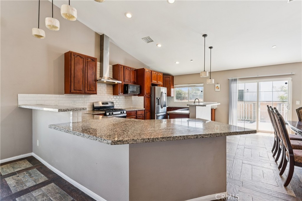 Open-plan kitchen with dark wood cabinets, granite peninsula, stainless appliances, and dining area by sliding doors.