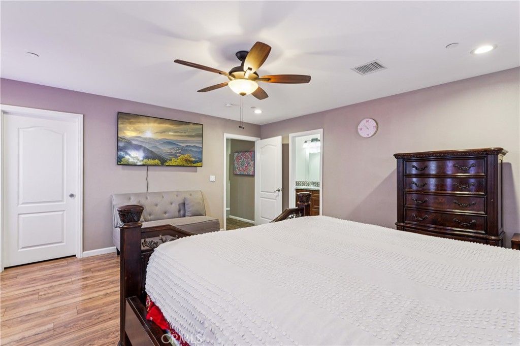 Furnished bedroom with a white textured bedspread, gray loveseat, dark wood dresser, and ceiling fan.