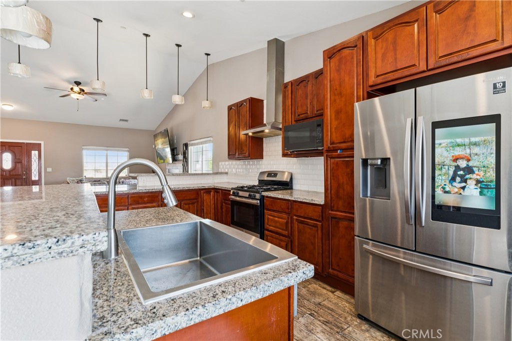 Kitchen with reddish-brown cabinets, granite island, double sink, and stainless steel appliances.