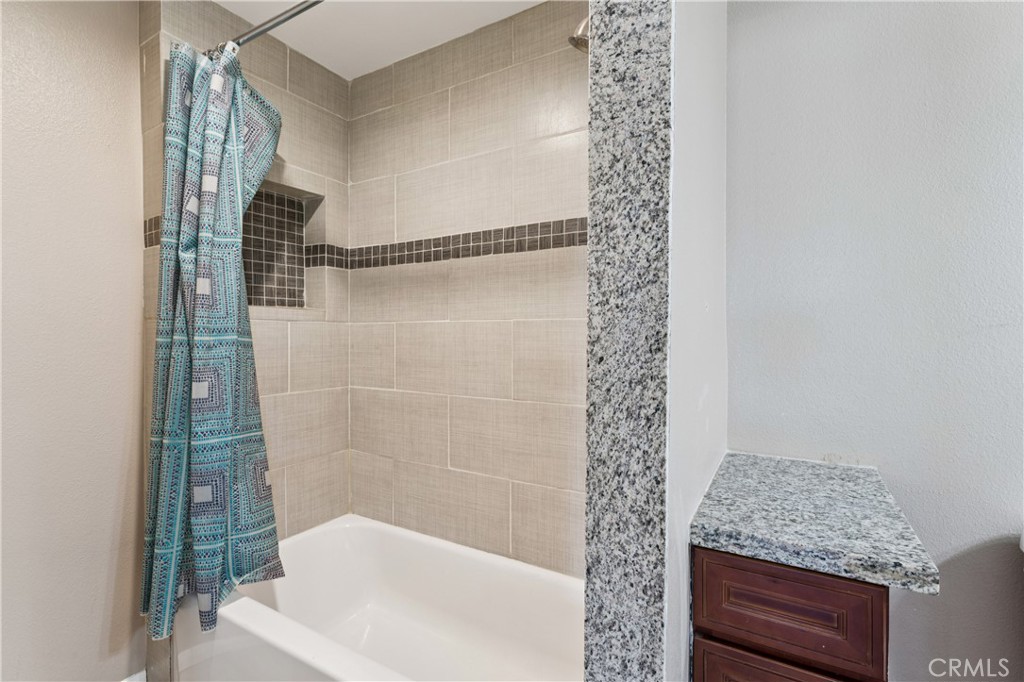 Bathroom with a tiled tub and shower, patterned blue curtain, granite partition, and dark wood vanity.