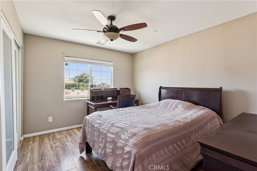 Bedroom with a dark wood bed, matching desk, ceiling fan, and window overlooking a dry landscape.