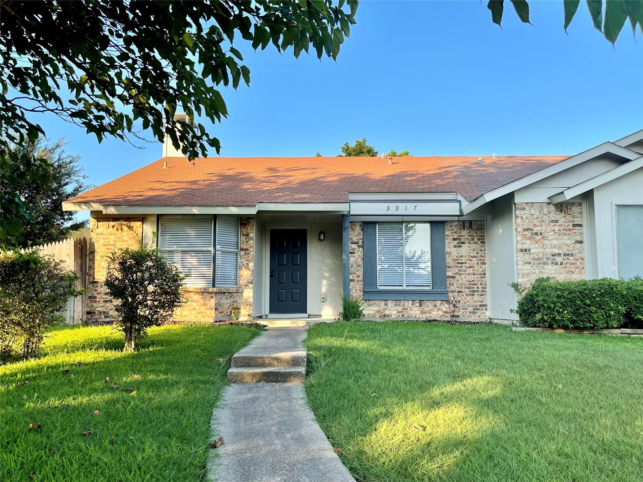 Single-story brick house with a blue front door, green lawn, and the number 3917 above the window.
