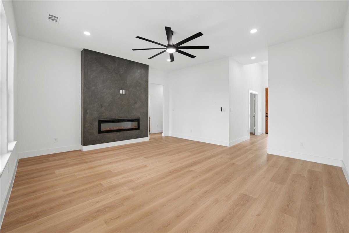 Vacant living room with a dark accent wall, linear fireplace, and light wood flooring.