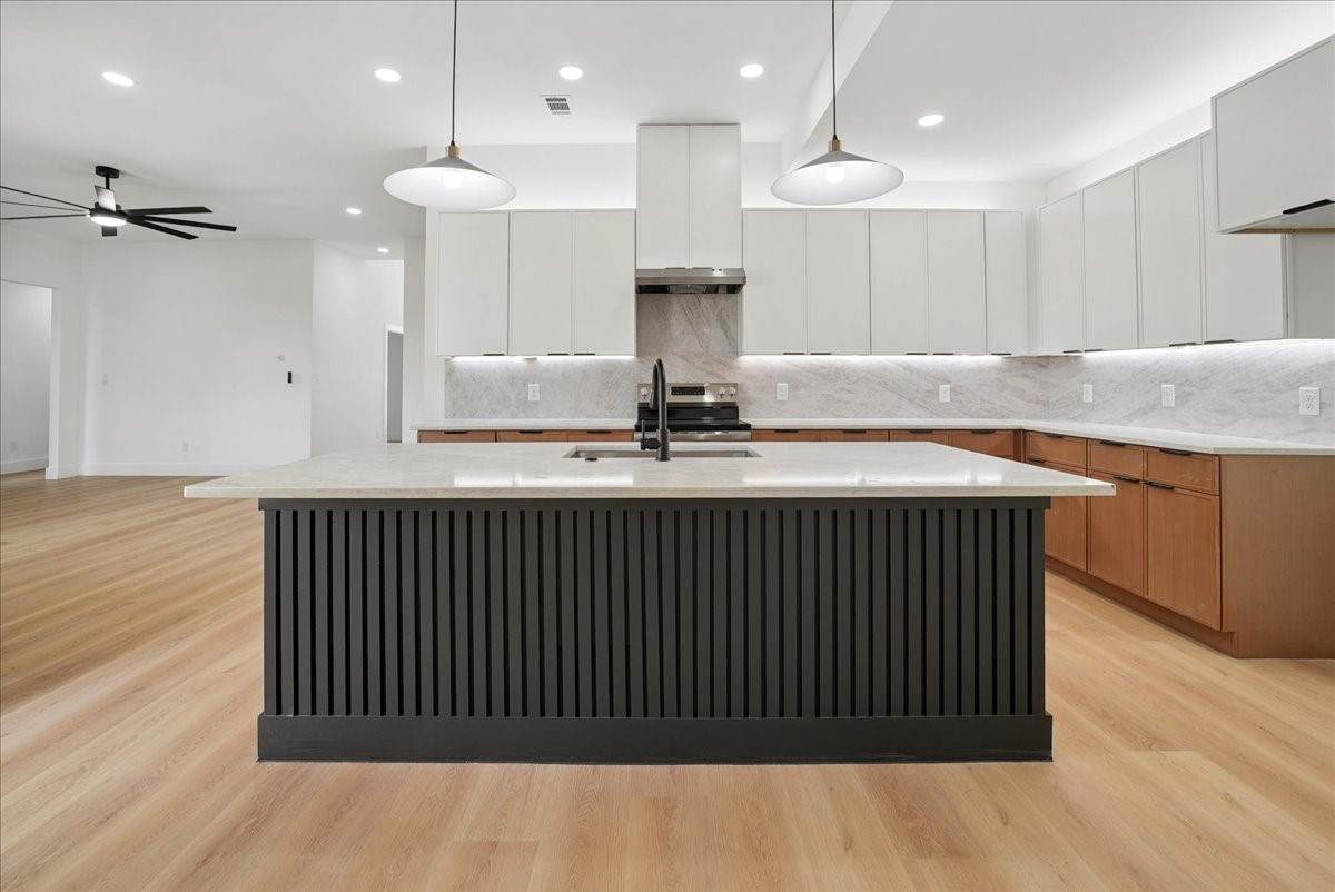 Vacant kitchen with a large black island, white cabinets, and warm wood flooring.