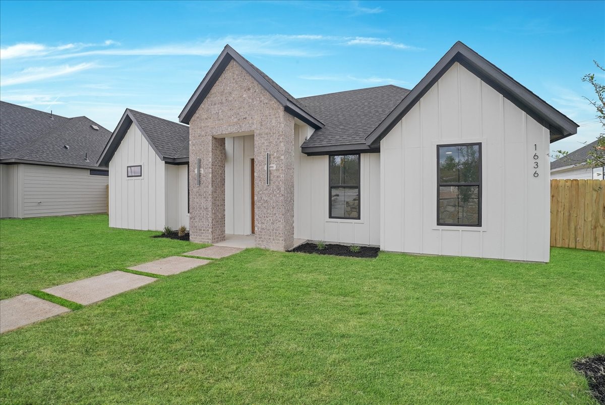 White single-story home with a brick-framed entry, dark gabled roof, and broad green lawn.