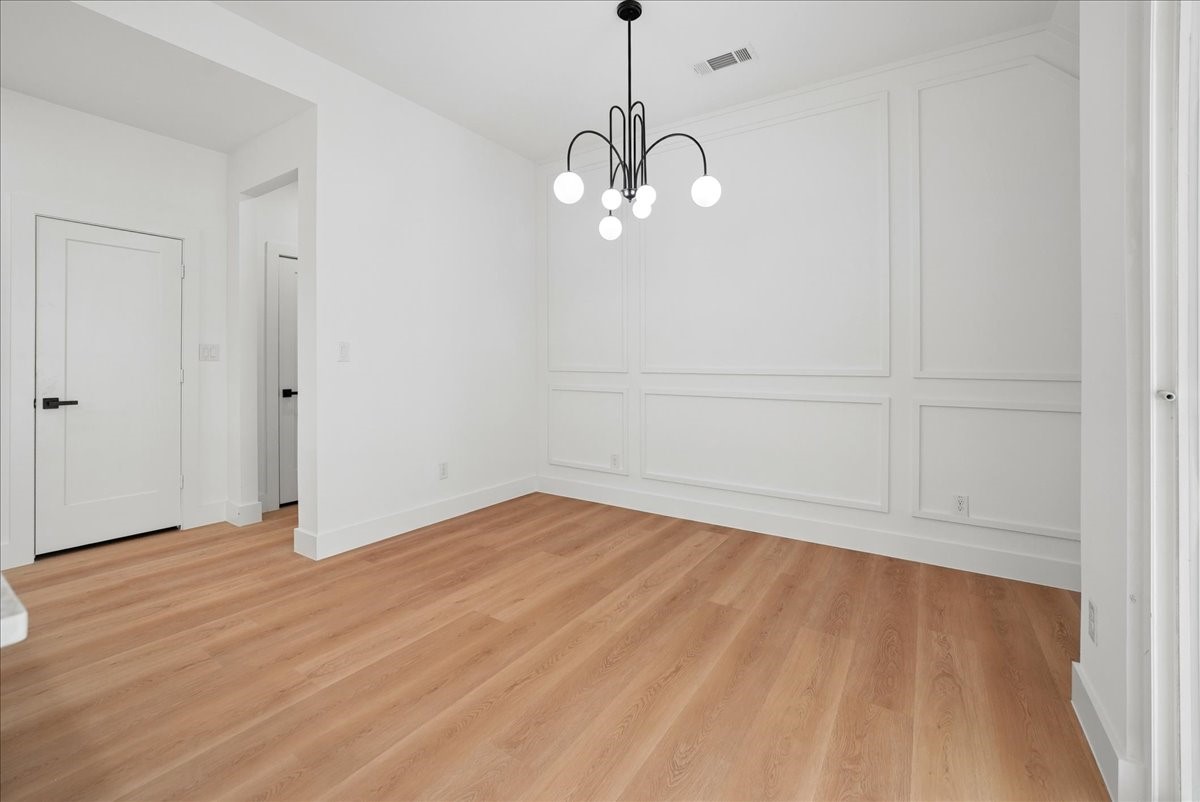 Empty dining room with wood floors, paneled walls, and a globe chandelier.