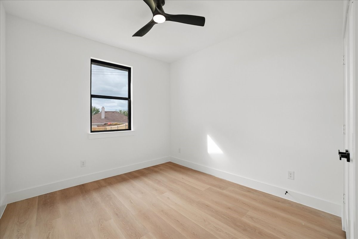 Empty bedroom with light wood floors, a black ceiling fan, and a single window.