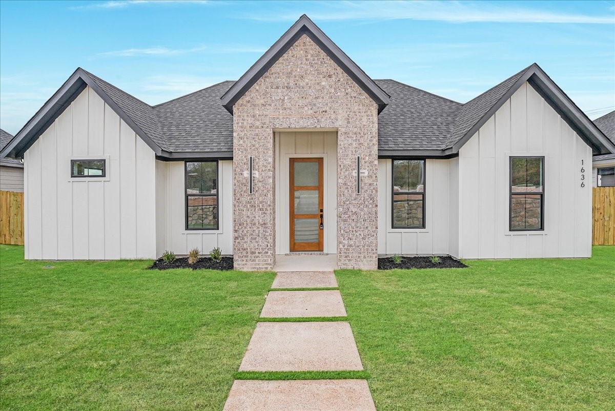 Single-story home with white siding, brick entry gable, and a walkway across the front lawn.