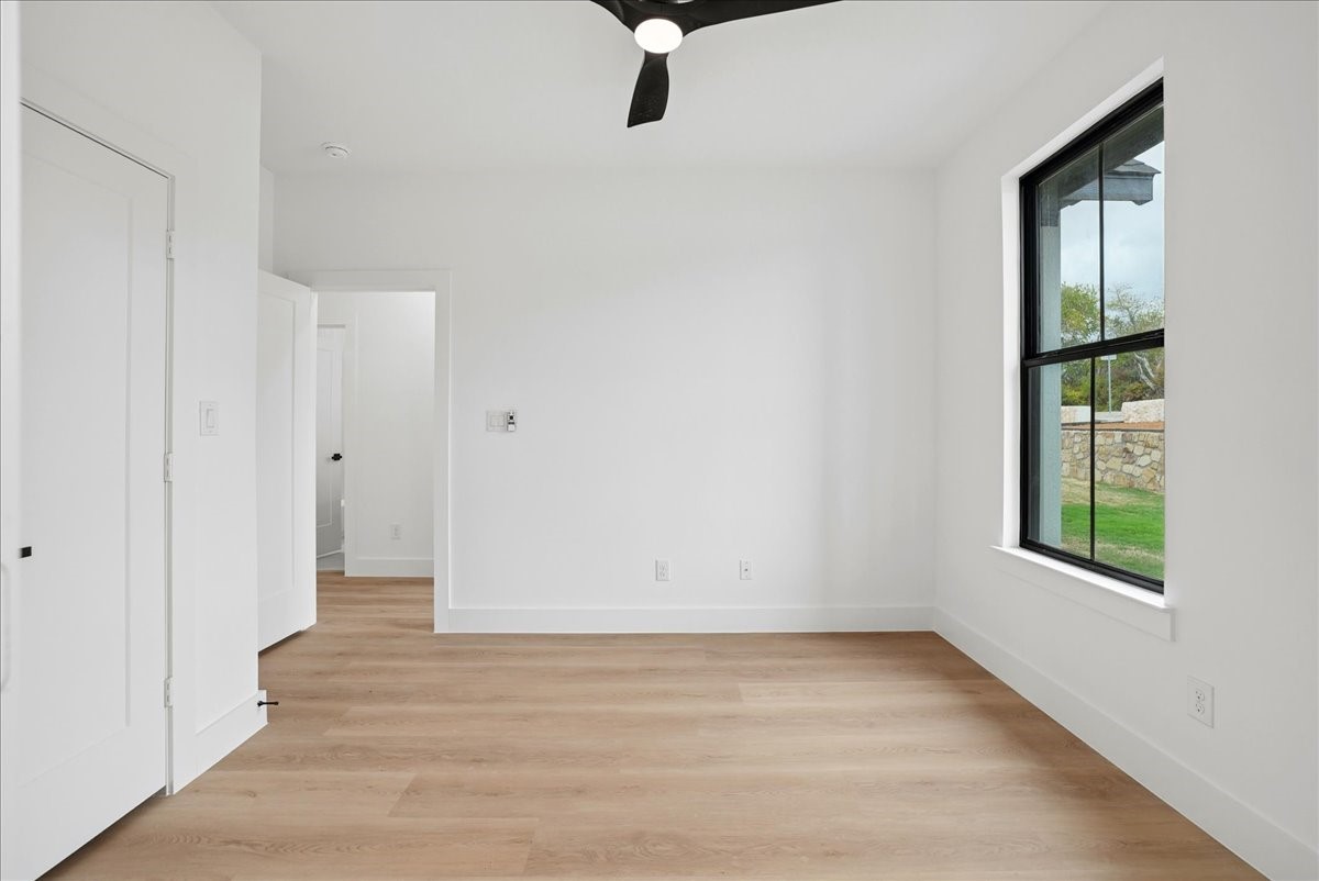 Empty bedroom with light wood flooring, ceiling fan, and large black-framed window.