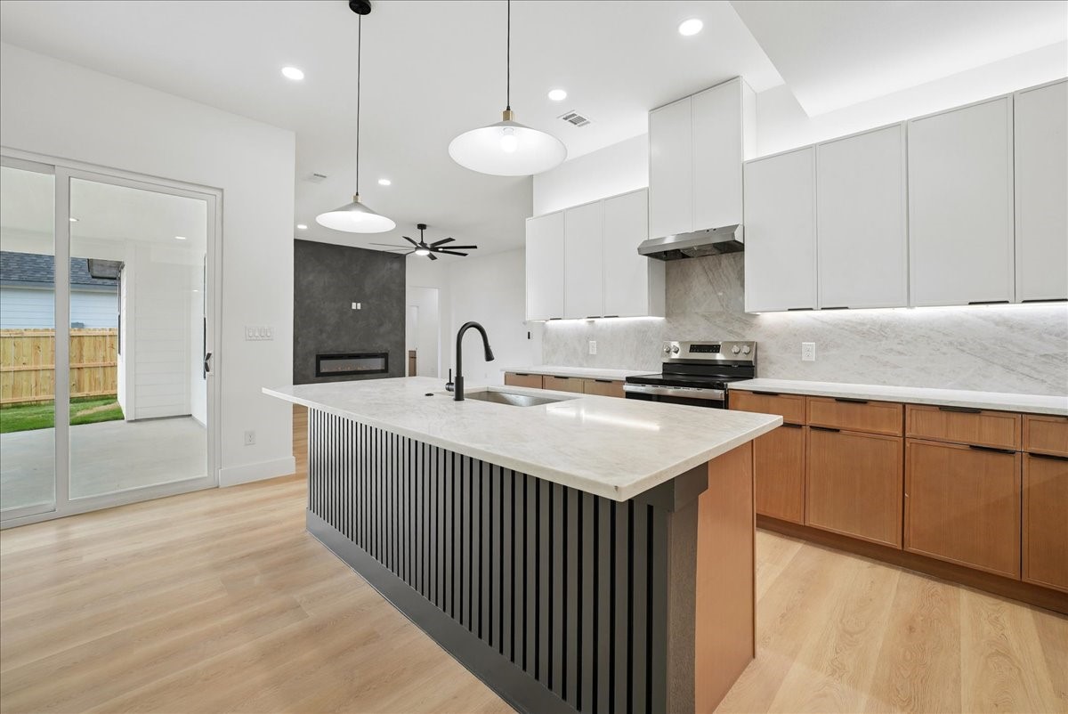 Modern kitchen with a large black-slat island, white counters, wood cabinets, and sliding doors to a patio.