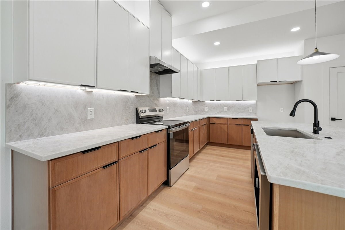 Modern kitchen with white cabinets, warm wood lower cabinets, and a large island with a black faucet.