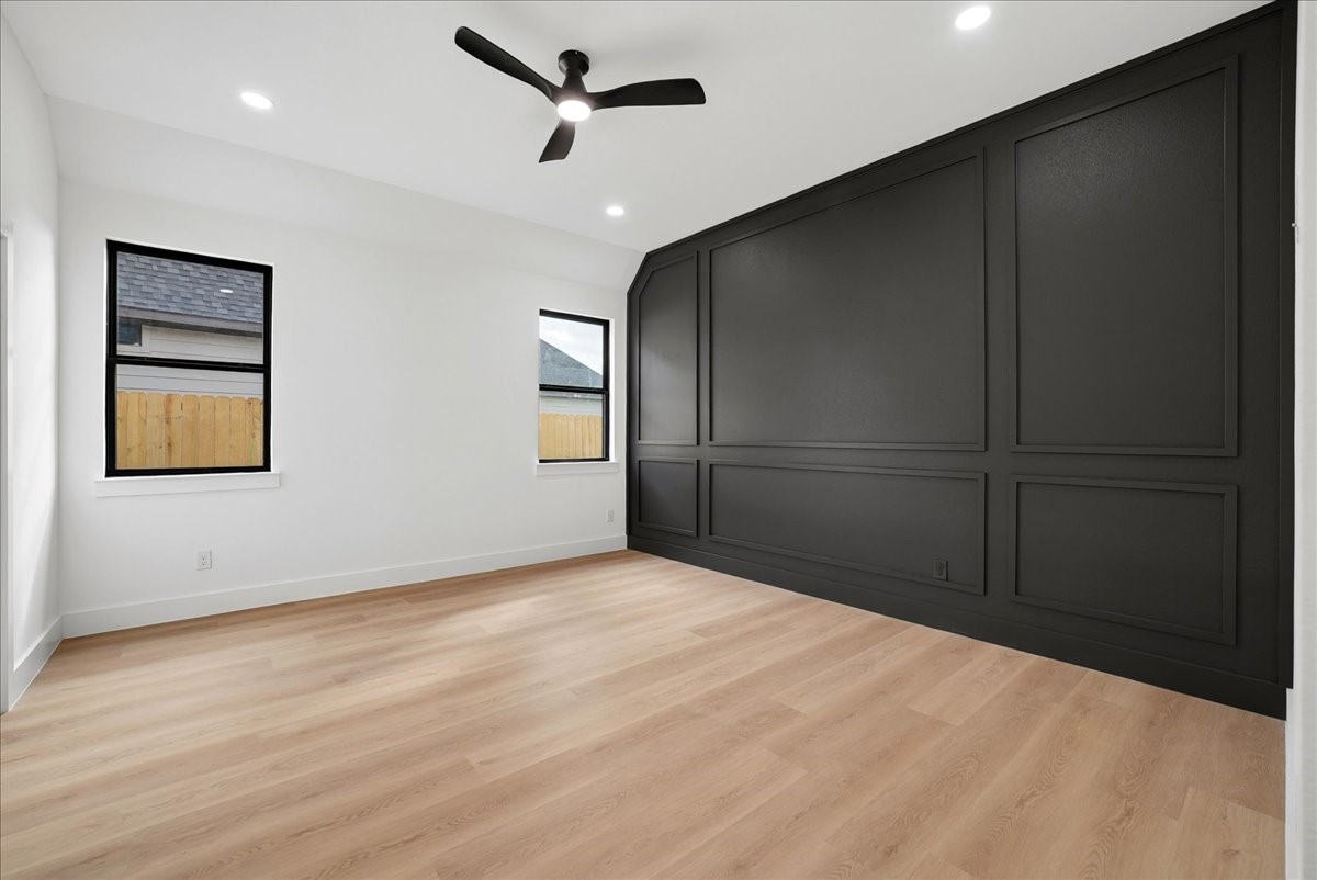 Empty bedroom with a dramatic black paneled wall and light wood floors.