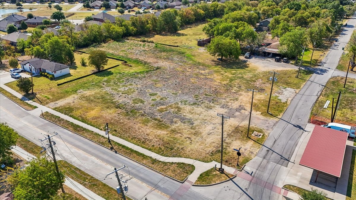 Vacant lot at a street intersection, bordered by homes, trees, and utility poles.