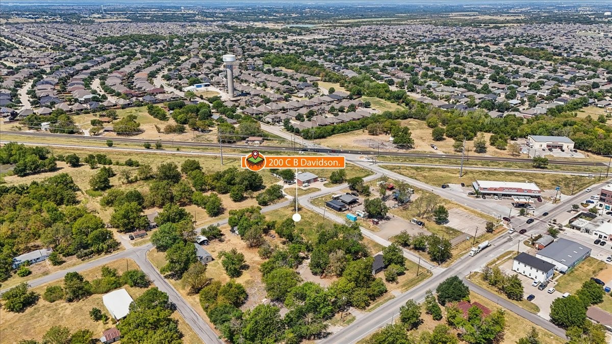Aerial view of the marked property beside a road, with open land and a residential neighborhood beyond.