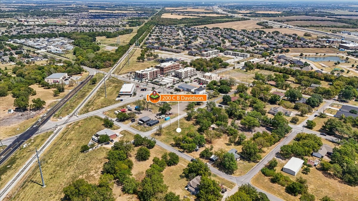 Aerial view of the marked property amid roads, open land, homes, and commercial buildings.