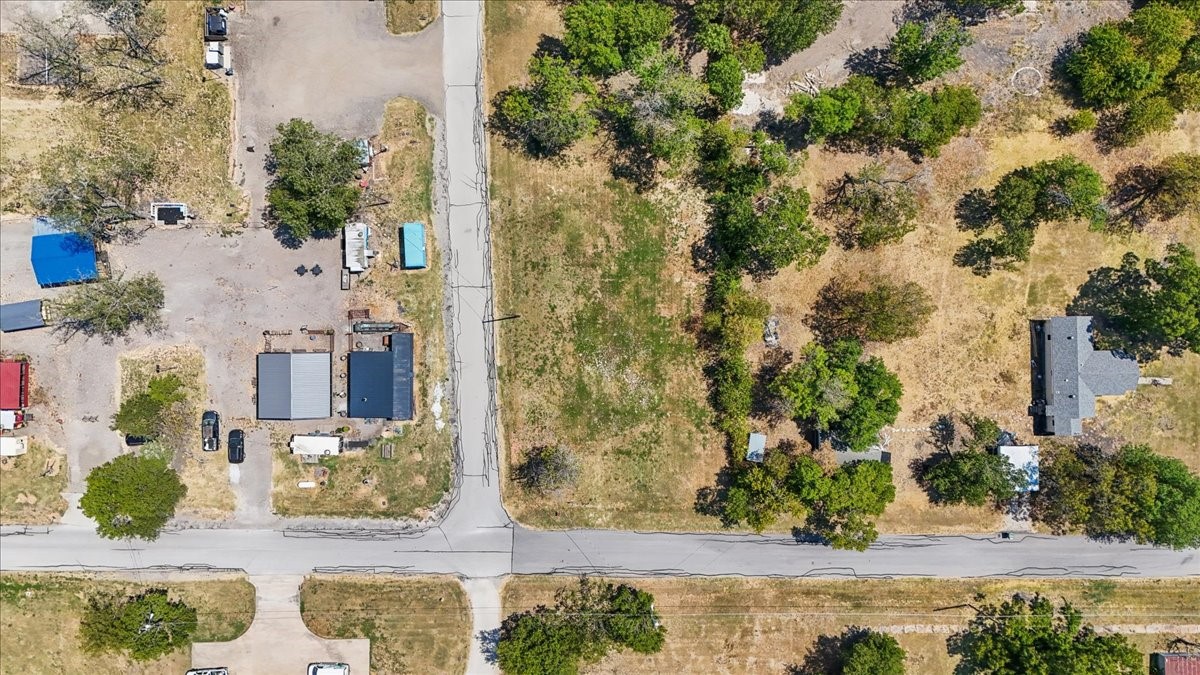Aerial view of a tree-dotted property with a detached house, outbuildings, and road frontage.