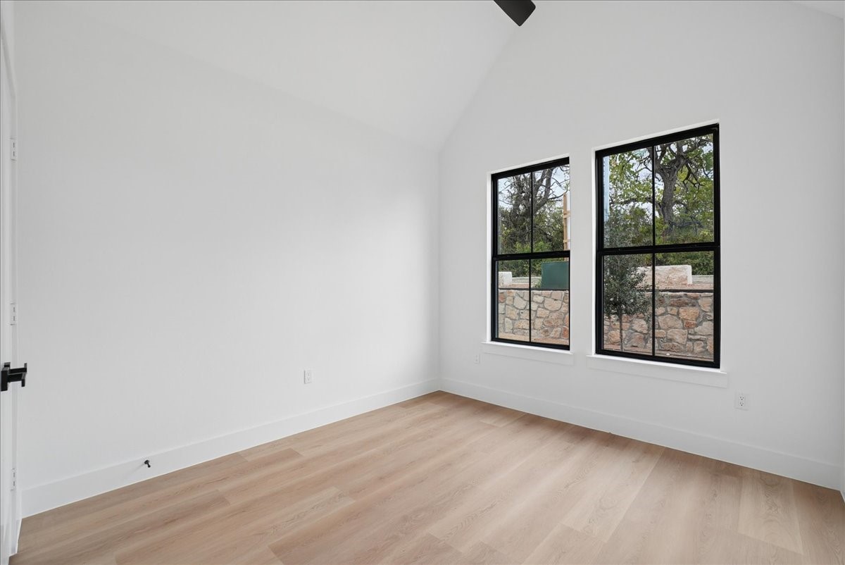 Empty interior room with light wood flooring and two black-framed windows.