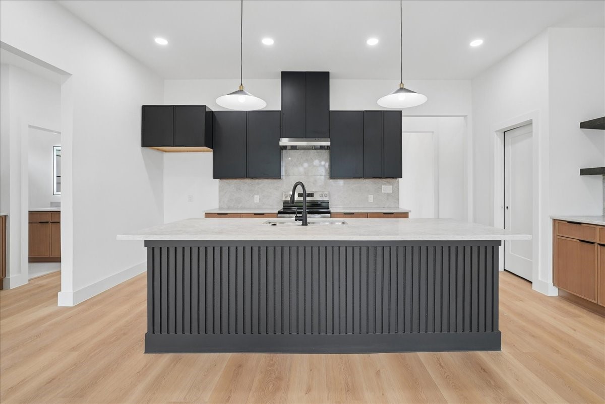 Modern kitchen with a large dark fluted island, black cabinets, and pale stone countertops.