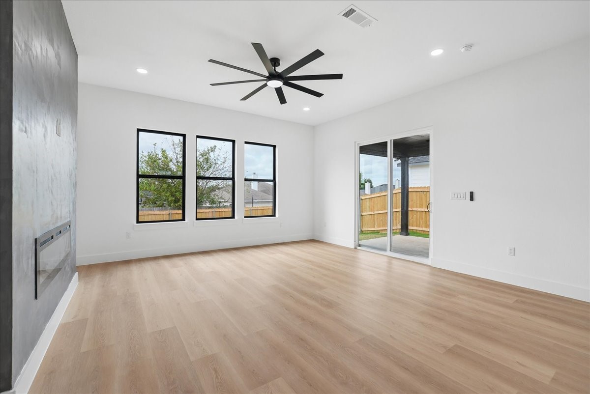 Empty living room with light wood floors, a gray fireplace wall, tall windows, and a sliding glass door.
