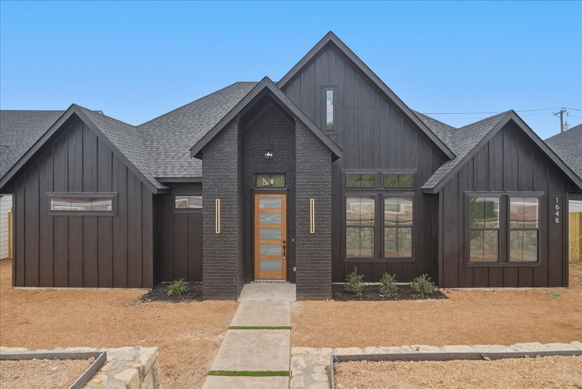 Modern dark-sided home with a brick entry, wood-and-glass door, and walkway.