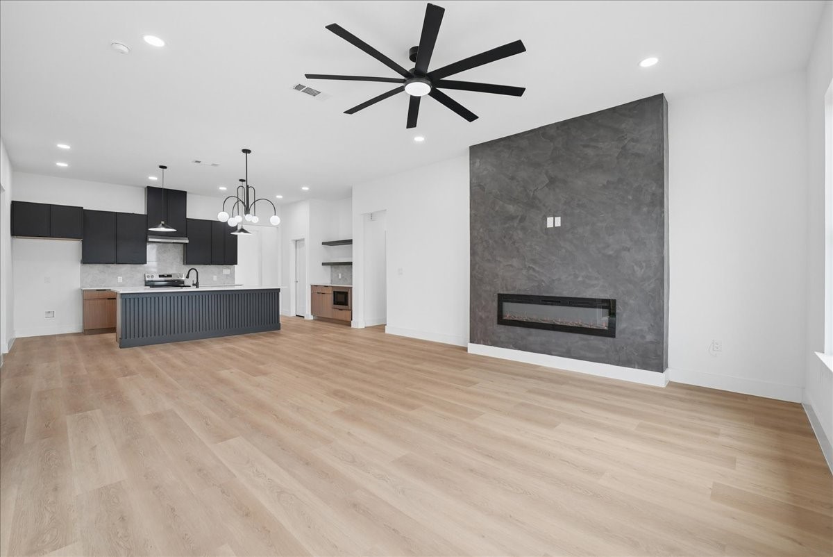Open kitchen and living area with a dark island, light wood floors, and a gray fireplace wall.