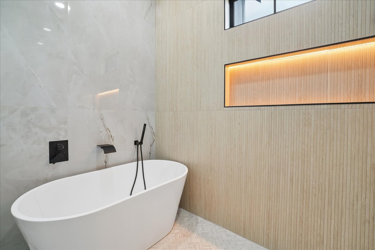 Modern bathroom with a freestanding soaking tub and illuminated niche in a wood-look wall.