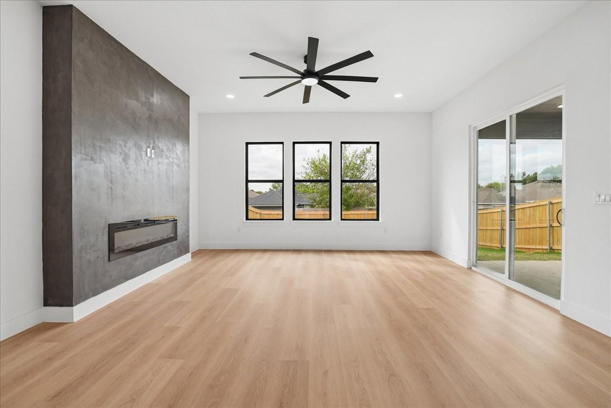 Empty living room with light wood floors, a dark concrete fireplace wall, and sliding glass doors to a fenced yard.