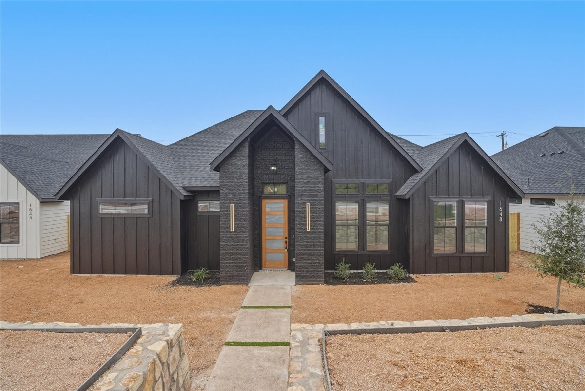 Modern dark-sided home with steep gables, brick entry, and a wood-and-glass front door.