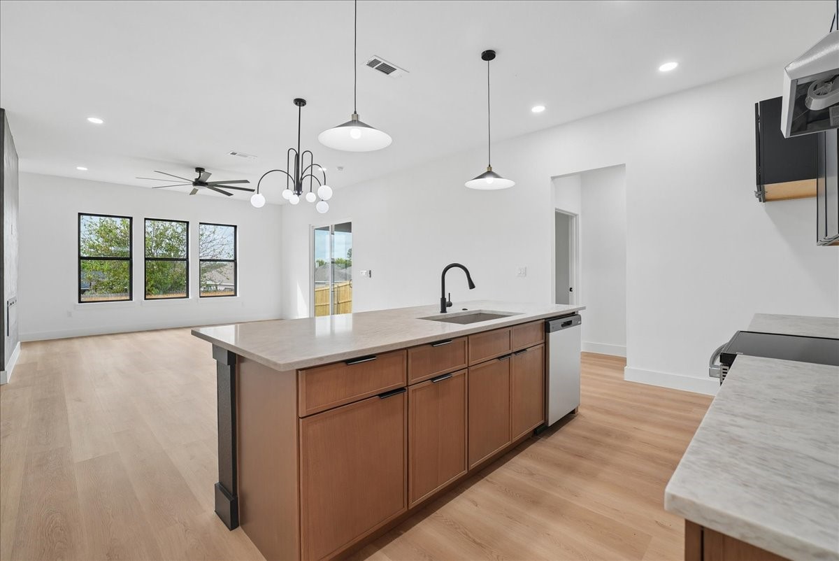 Open kitchen with a large wood-cabinet island, stone counters, pendant lights, and three windows.