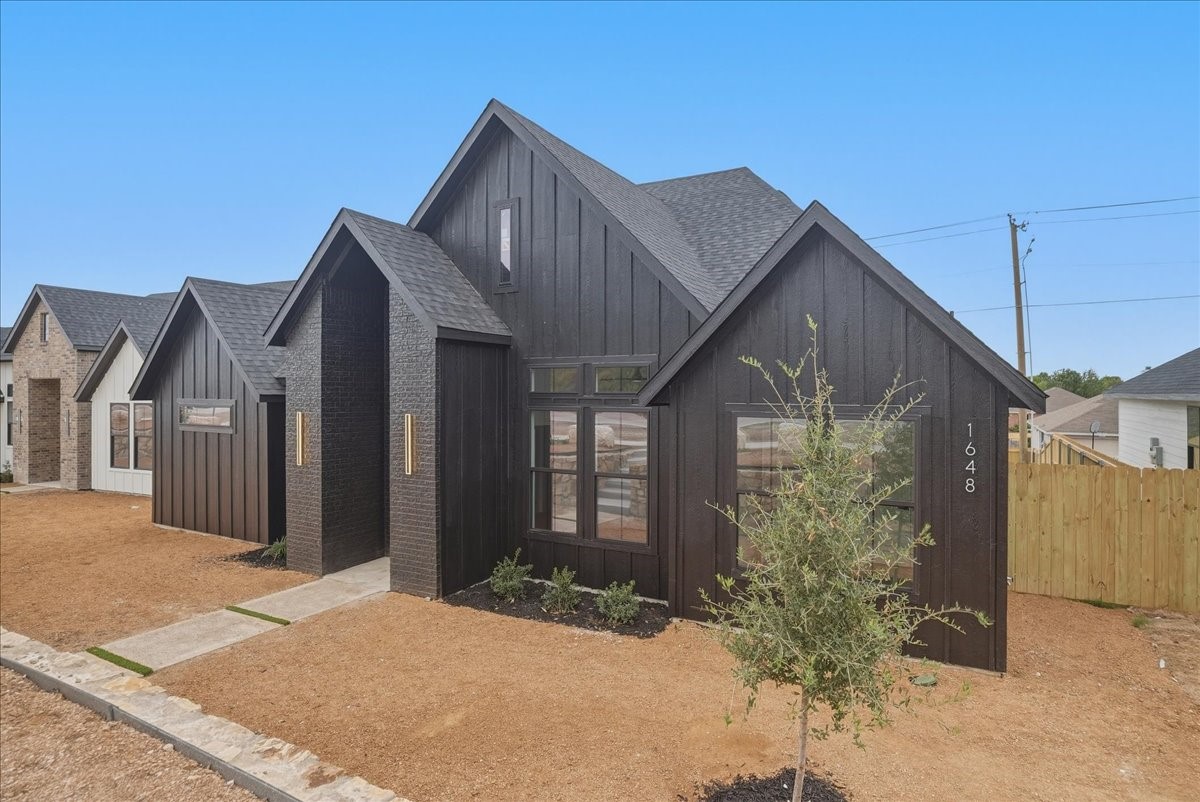 Modern dark-sided home with steep gables, black brick accents, and a young tree in the bare front yard.