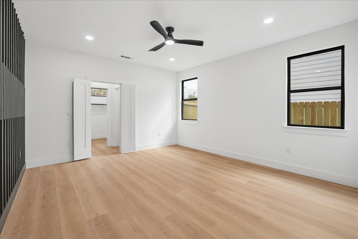 Empty bedroom with light wood floors, a black ceiling fan, and an open closet.