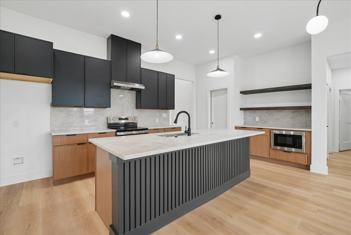 Modern kitchen with a large black fluted island, dark cabinets, and warm wood flooring.