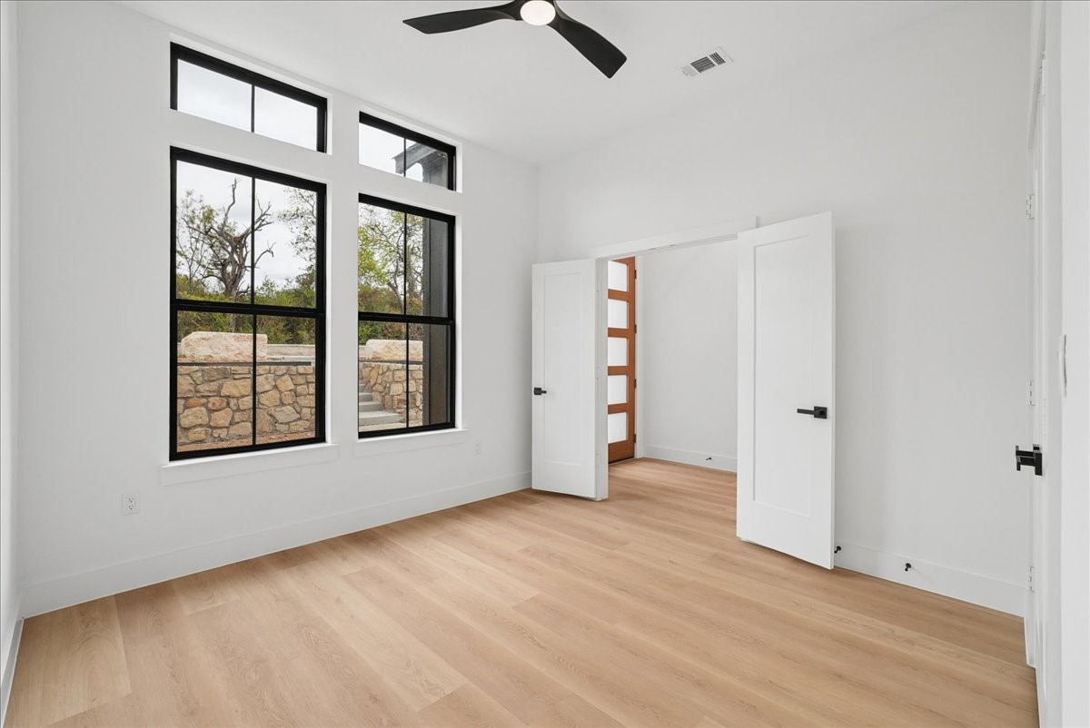 Empty room with light wood floors, tall black-framed windows, and open double doors.