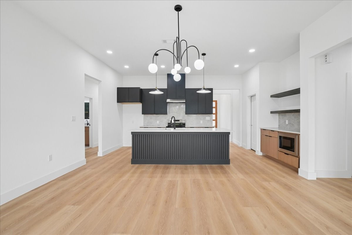 Open kitchen with a charcoal island, dark cabinets, light wood floors, and a modern globe chandelier.