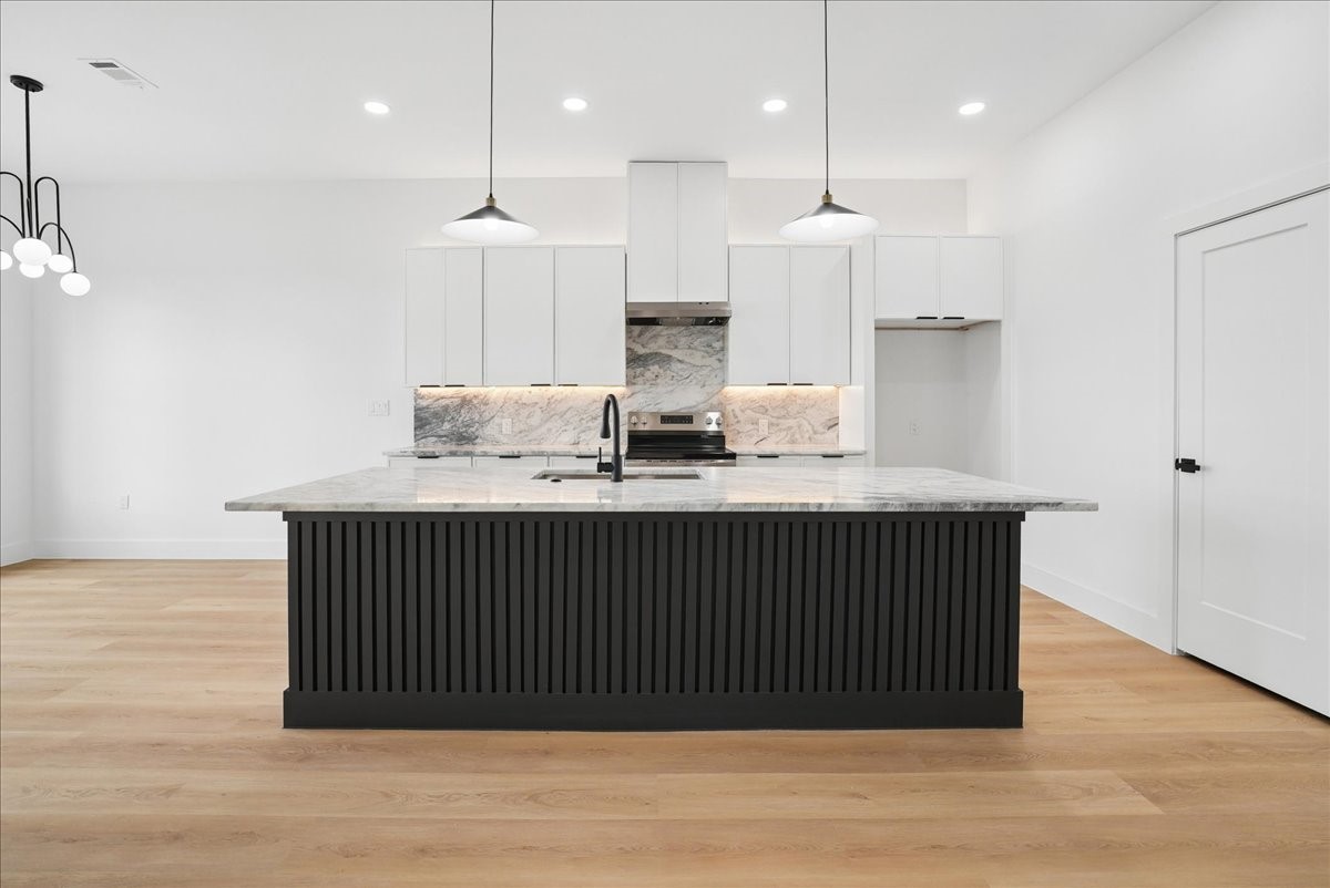 Modern kitchen with a large black fluted island, marble surfaces, white cabinetry, and light wood floors.